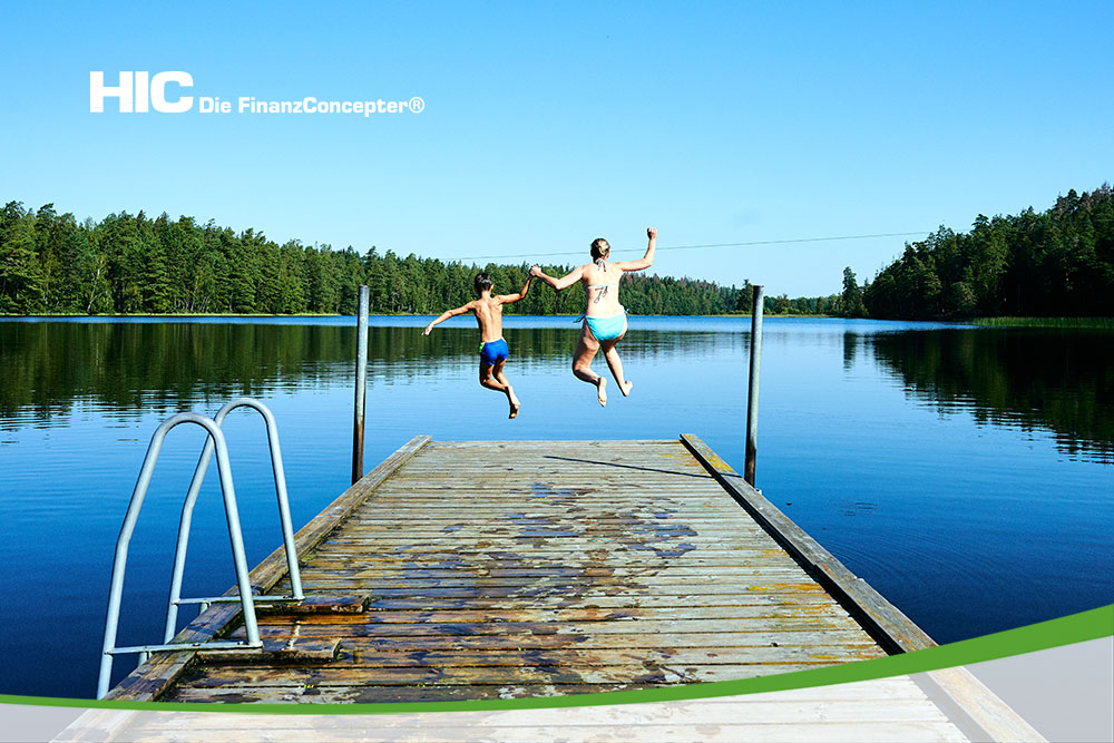 Eine Frau und ein Junge springen von einem Steg in einen Waldsee.