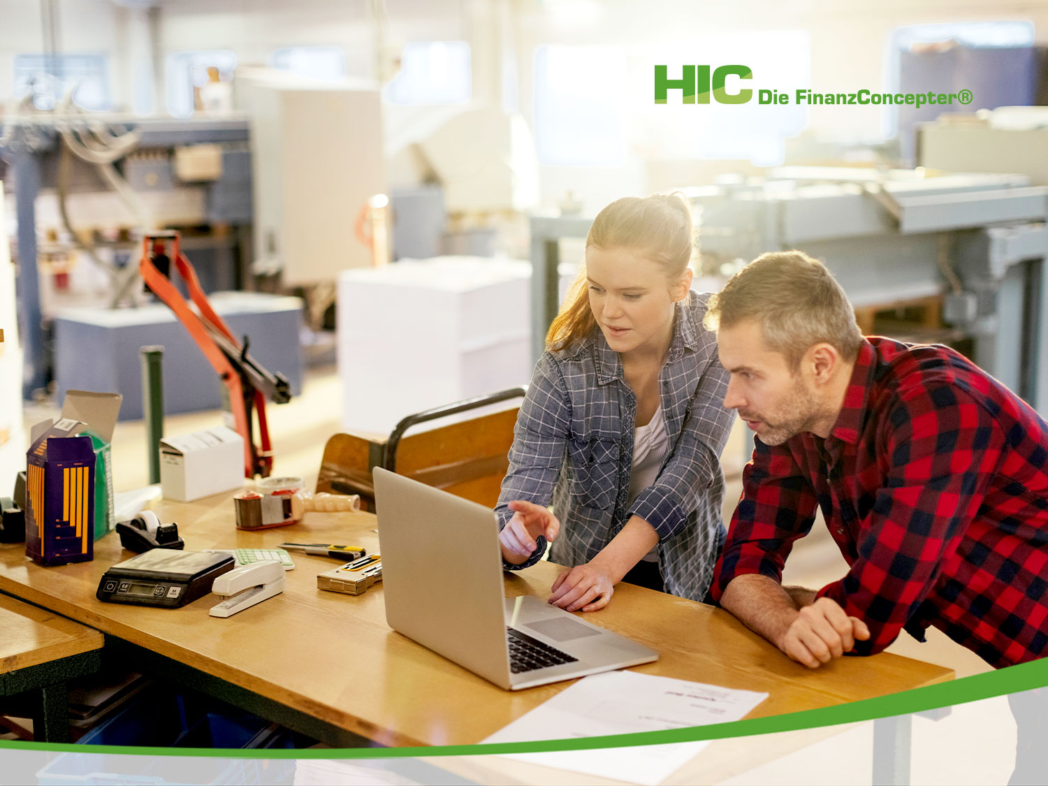 In einer Werkhalle zeigt eine junge Frau einem Kollegen etwas auf ihrem Laptop.