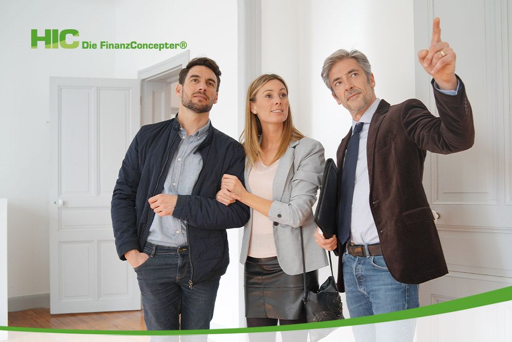  Ein Immobilienberater im Anzug zeigt einem jungen Paar eine helle Wohnung und deutet mit dem Finger nach oben. Das Paar schaut interessiert in die gezeigte Richtung. Oben links befindet sich das Firmenlogo von „HIC Die FinanzConcepter“